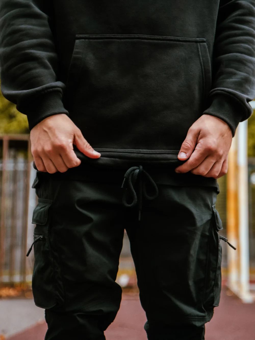 Model adjusting the bottom hem drawstrings of the black RHSM MVMT Hoodie for a secure, custom fit.