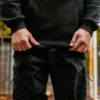 Model adjusting the bottom hem drawstrings of the black RHSM MVMT Hoodie for a secure, custom fit.