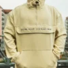 A close-up of a model with hands in the spacious front pouch of the beige RHSM MVMT Hoodie.