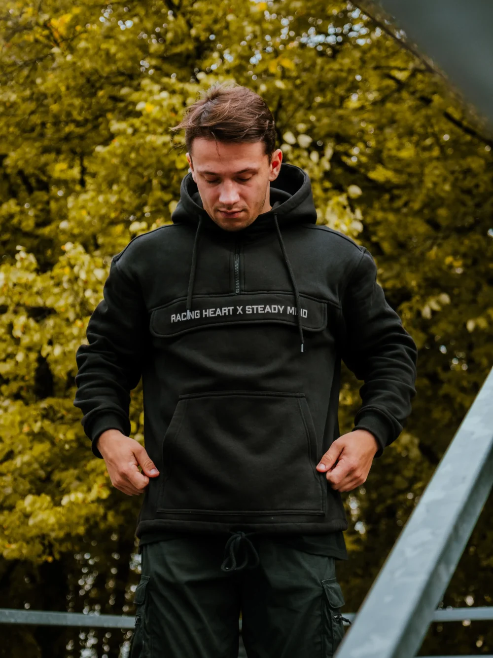 Model showcasing the spacious front kangaroo pocket of the black RHSM MVMT Hoodie.