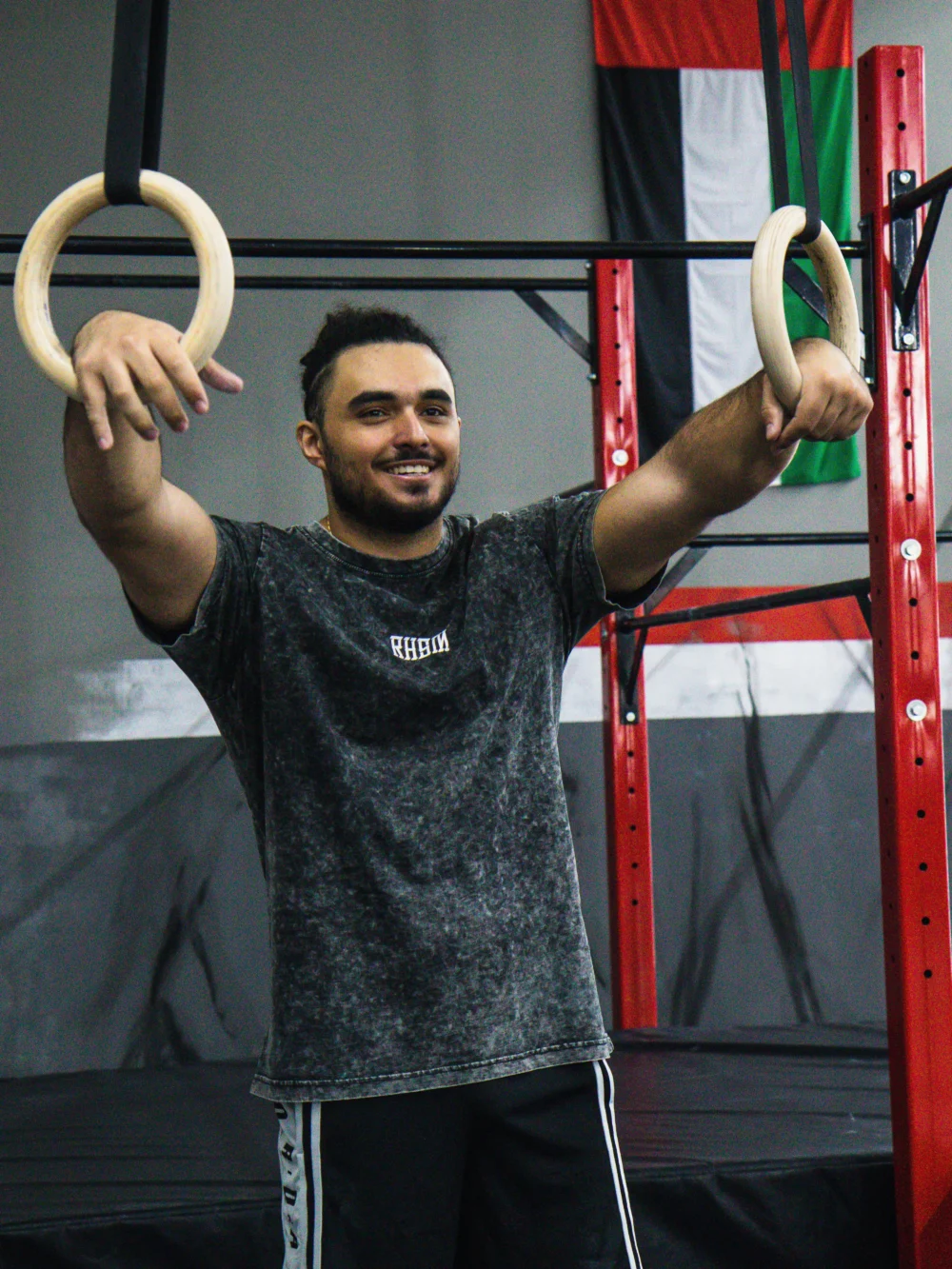 A model wearing the RHSM Acid Wash Tee in a gym setting near a pair of gymnastic rings.
