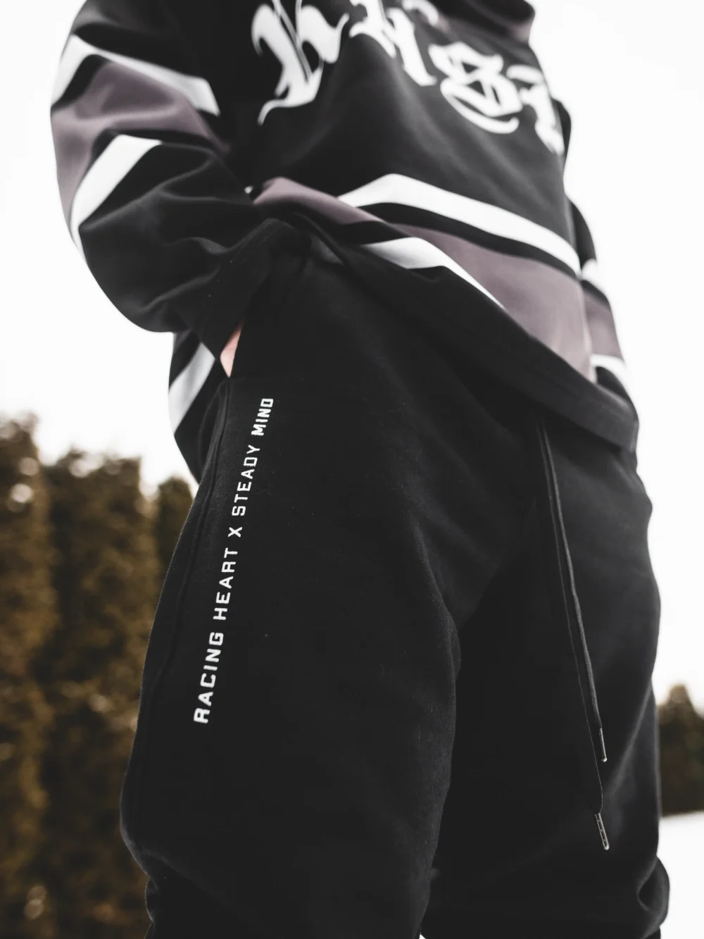 A full view of a model wearing the black RHSM Classic Fit Sweatpants in an outdoor setting, showcasing their versatile streetwear and training style.