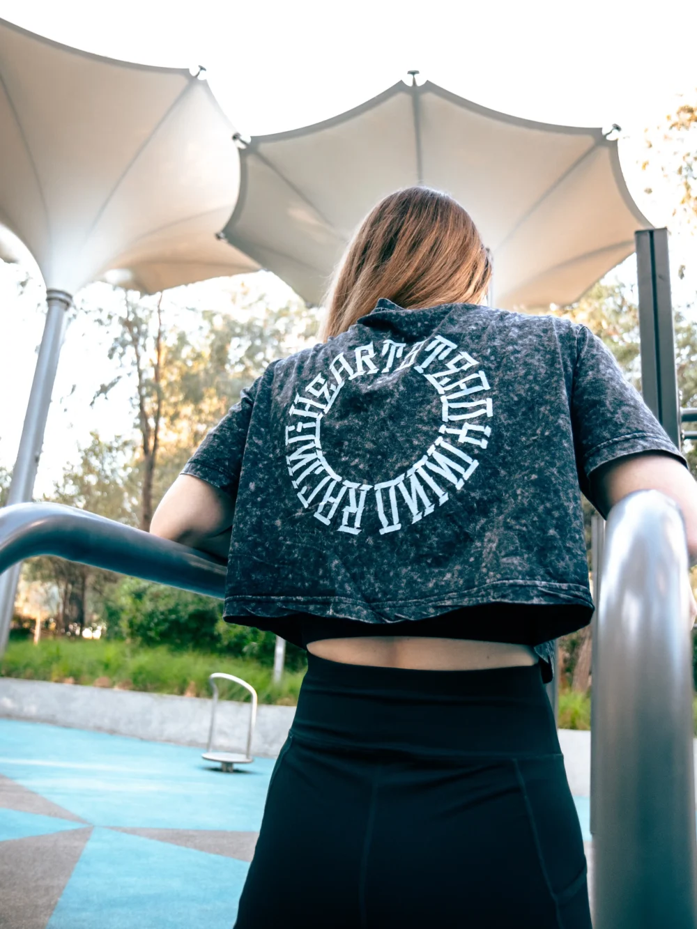 An athlete wearing the RHSM Acid Wash Crop-Top at an outdoor calisthenics park, showing the back graphic.