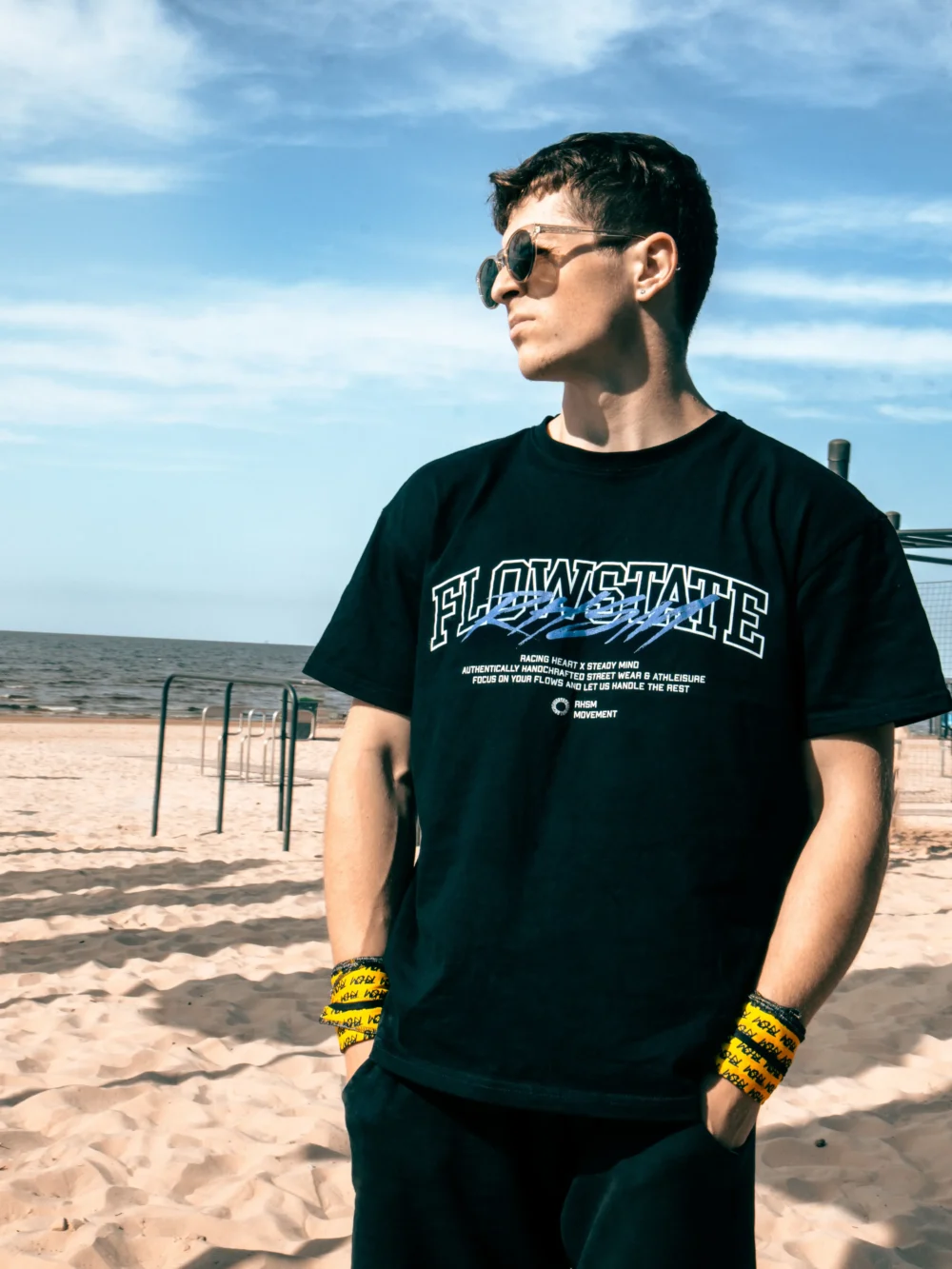 Model wearing the oversized black RHSM Flowstate Tee at the beach, showcasing its streetwear style.