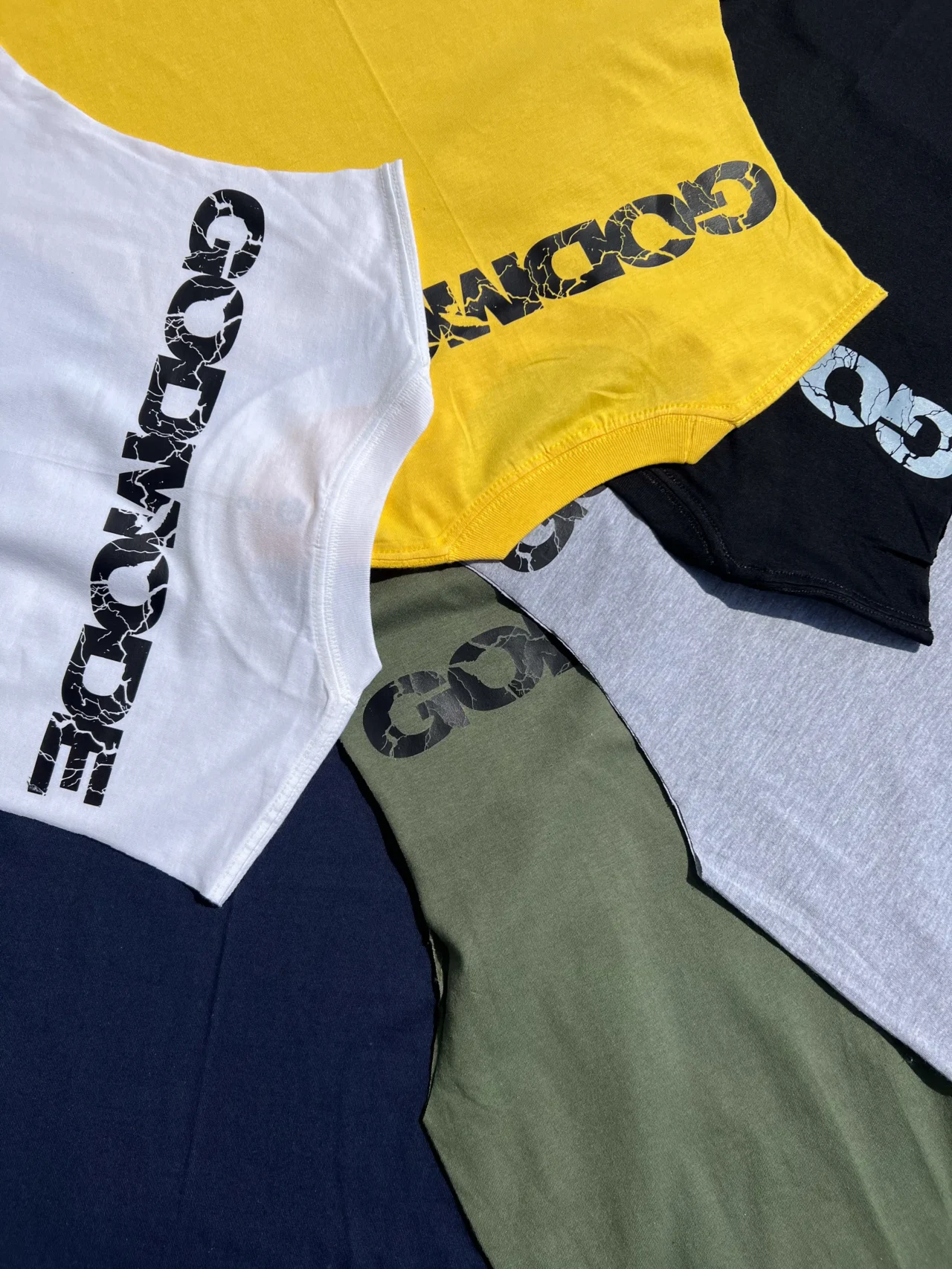 A stack of all available colorways of the RHSM Godmode Tank Top, including black, white, gray, khaki, blue, and yellow.