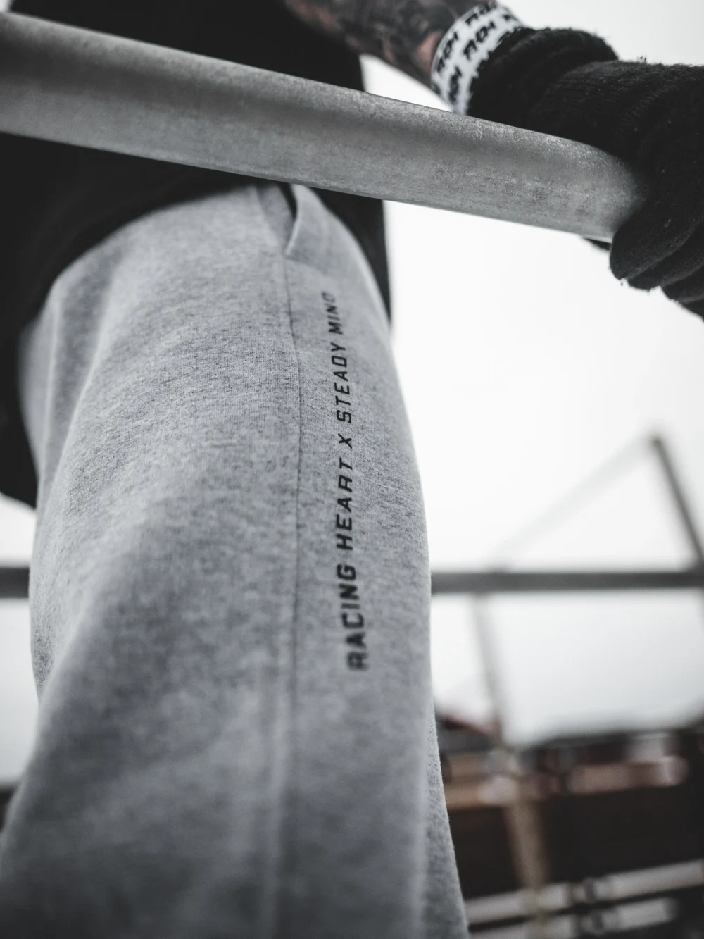 An outdoor close-up of the "Racing Heart X Steady Mind" graphic on the gray RHSM Classic Fit Sweatpants, worn by a model.