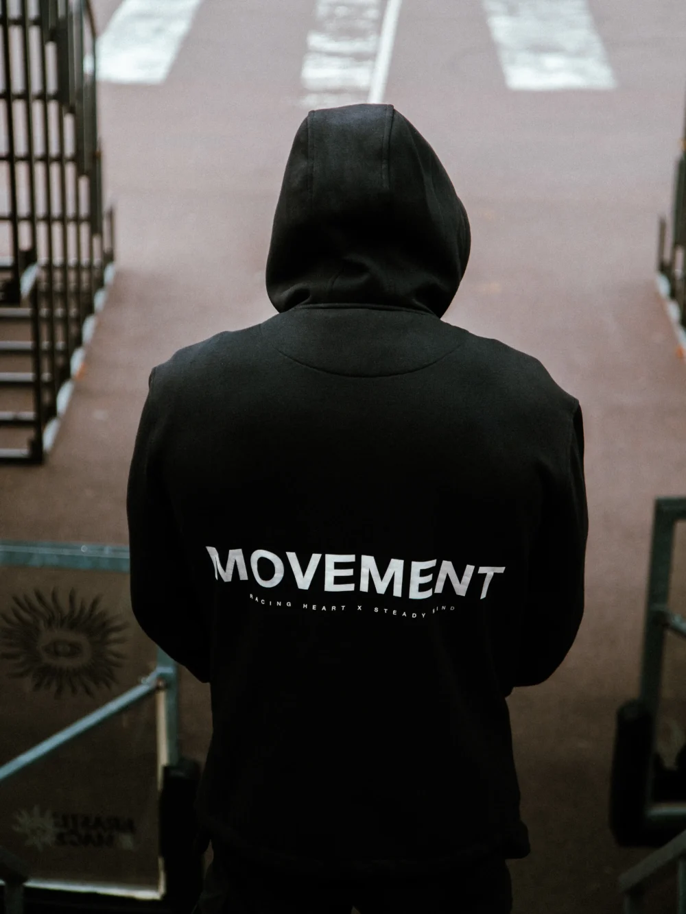 An athlete wearing the black RHSM MVMT Hoodie in an urban setting, highlighting its streetwear aesthetic.