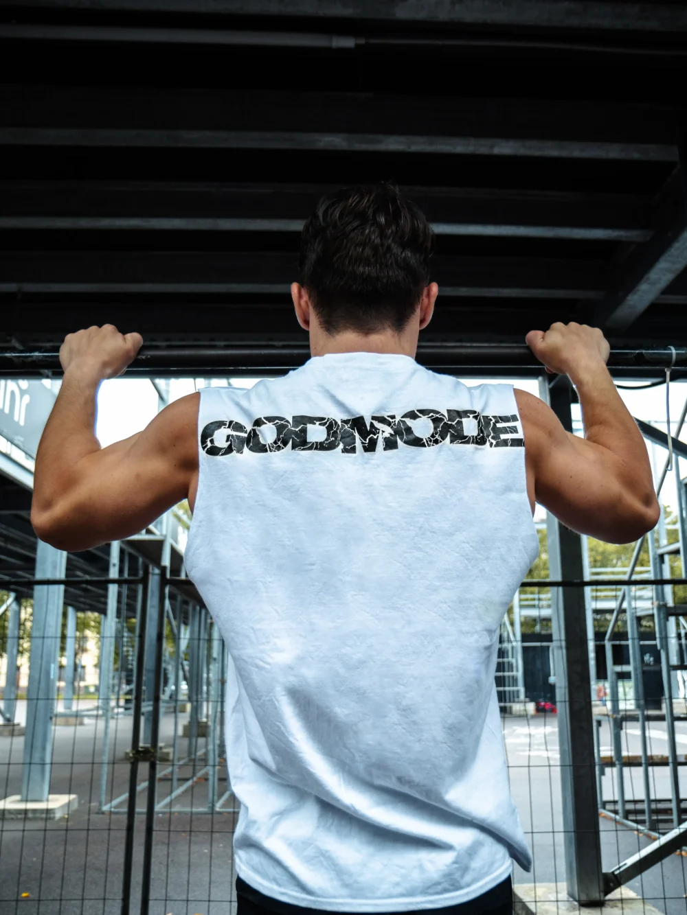 An athlete performing a pull-up while wearing the white RHSM Godmode Tank Top, showing the back graphic in action.