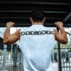 An athlete performing a pull-up while wearing the white RHSM Godmode Tank Top, showing the back graphic in action.