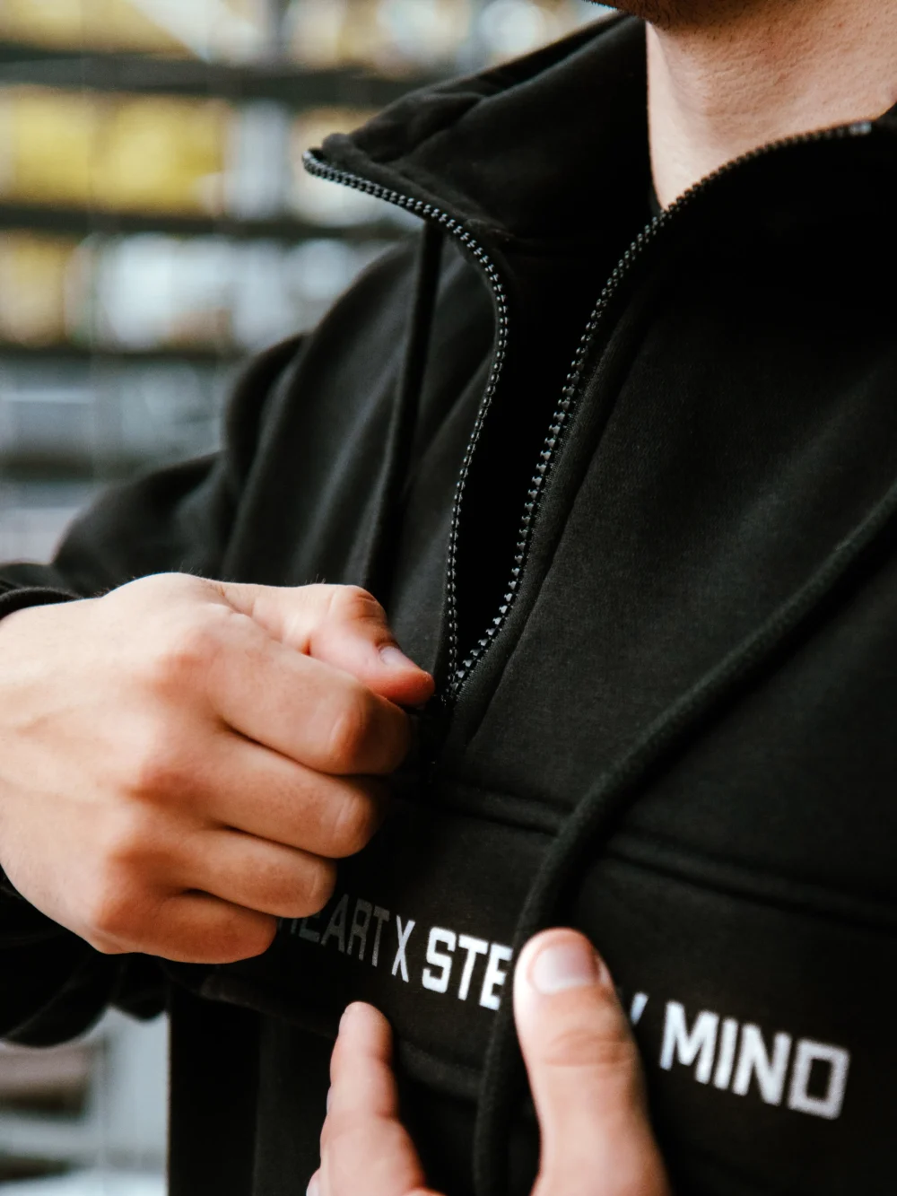 Detailed close-up of the secure zipper on the front pocket of the black RHSM MVMT Hoodie.