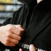 Detailed close-up of the secure zipper on the front pocket of the black RHSM MVMT Hoodie.
