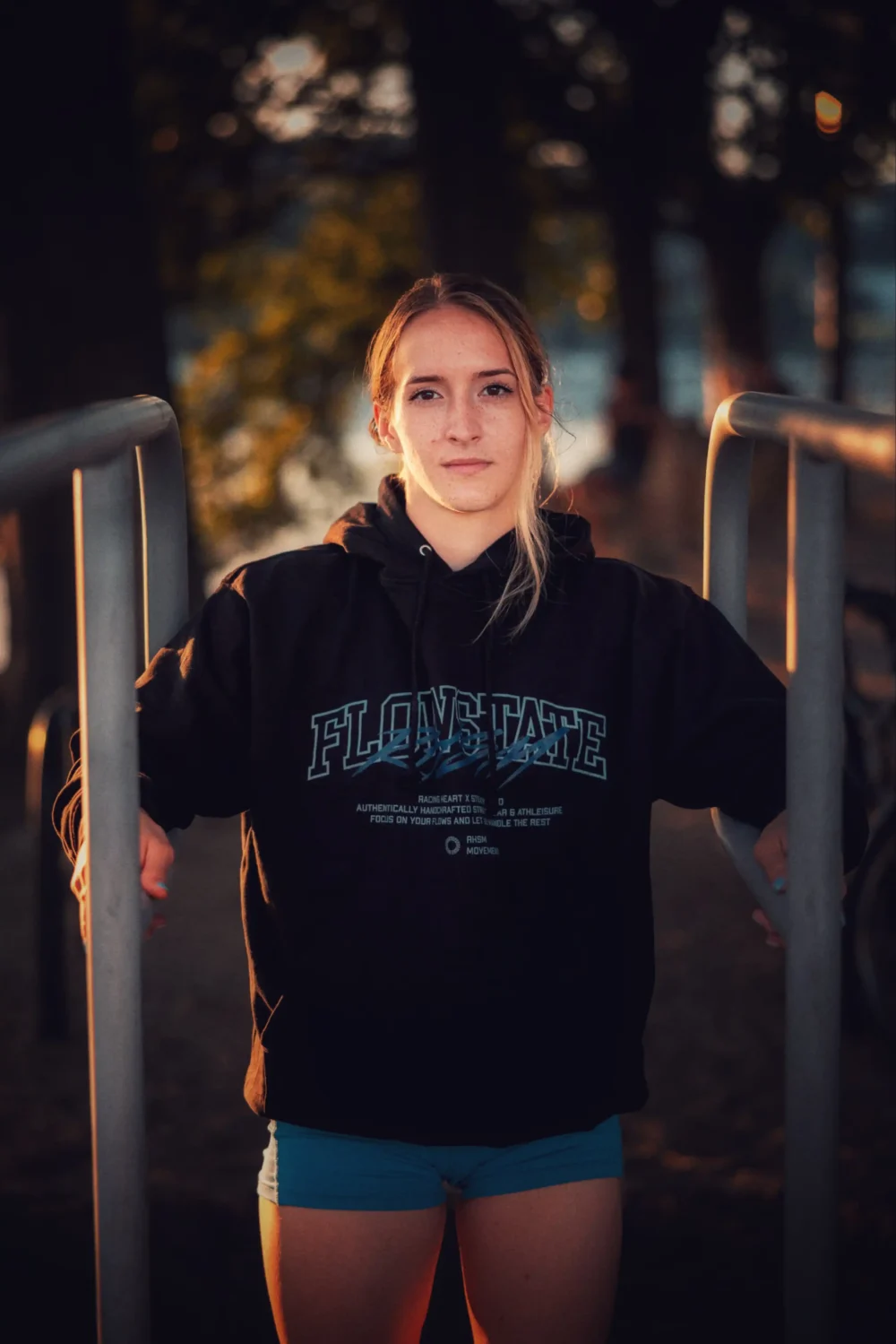 An athlete wearing the black RHSM Flowstate Hoodie while preparing for a workout at calisthenics bars.