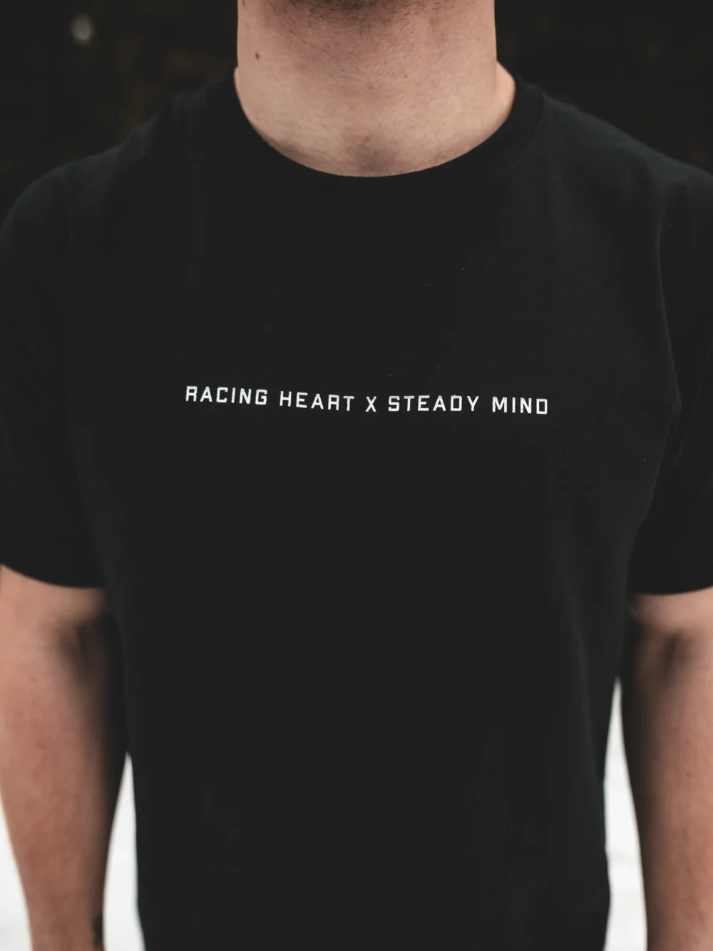 An outdoor close-up of the minimalist design on the black RHSM Classic Fit Tee, worn by a model.
