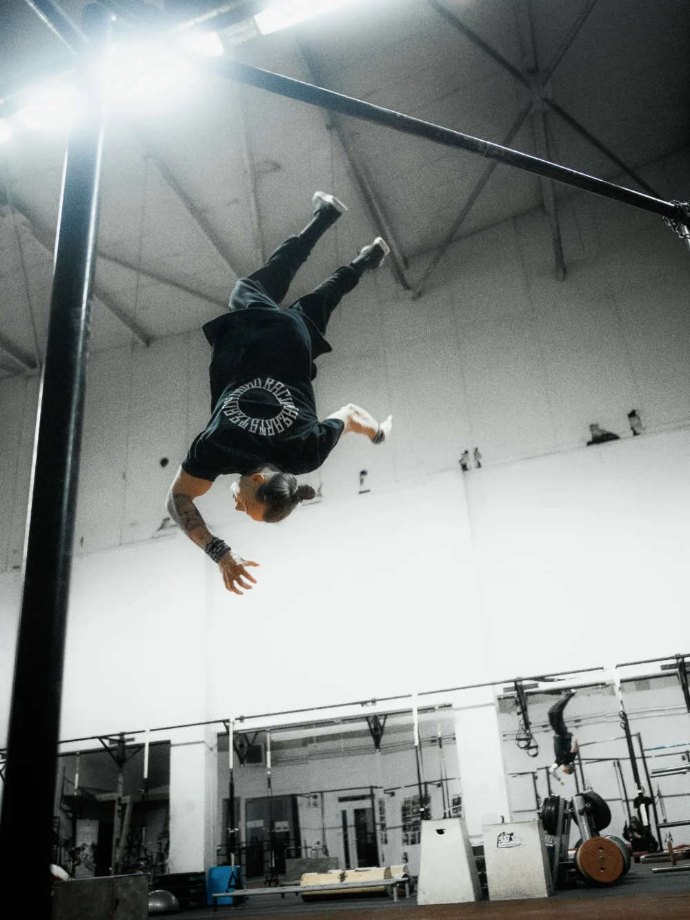 Pro athlete Daniels Laizans doing a backflip from a bar in the black RHSM Long Fit Tee V2.