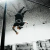 Pro athlete Daniels Laizans doing a backflip from a bar in the black RHSM Long Fit Tee V2.