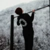Back view of an athlete doing a pull-up in the black RHSM Long Fit Tee V2, showing the back graphic during a workout.