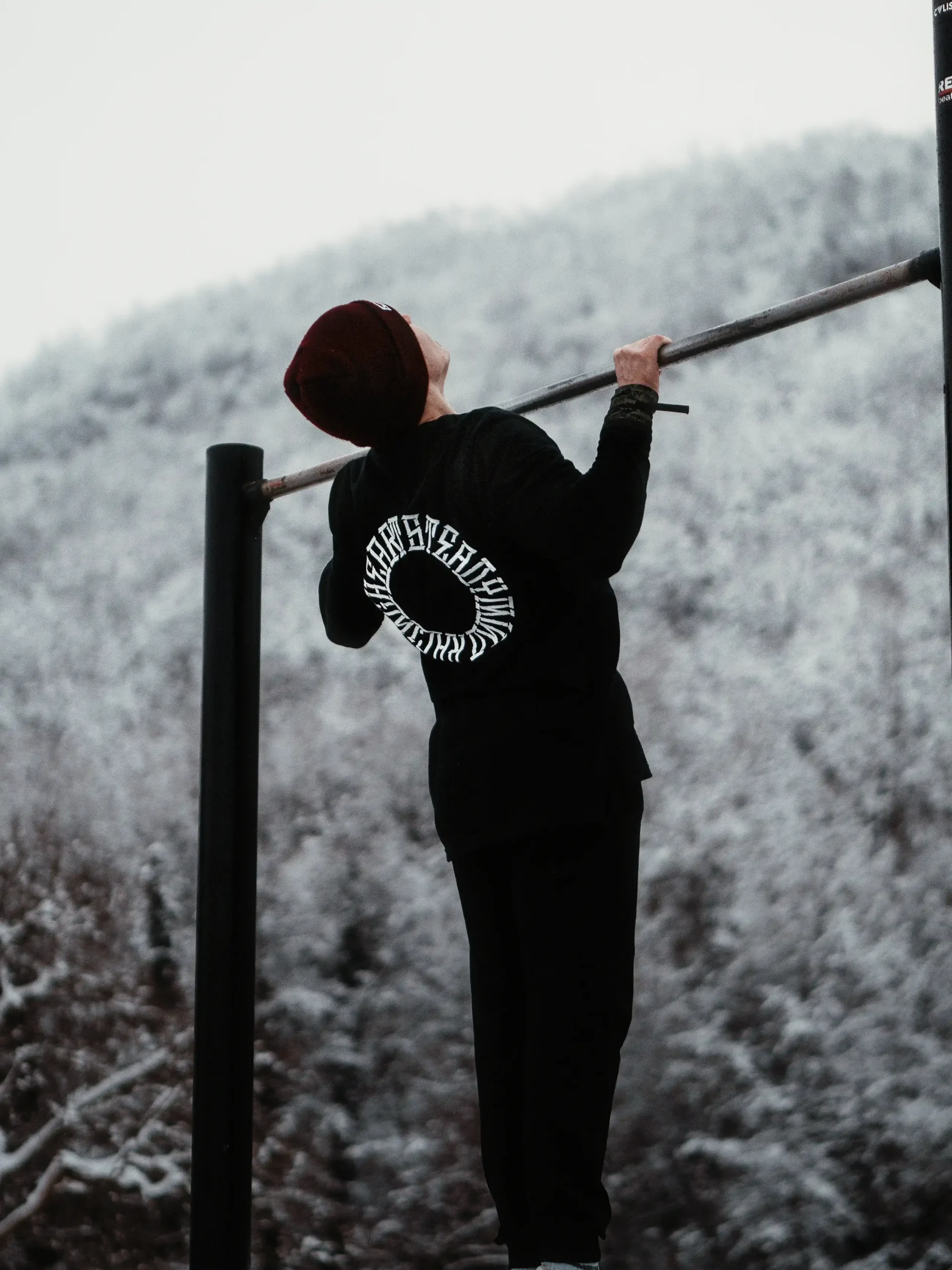Back view of an athlete doing a pull-up in the black RHSM Long Fit Tee V2, showing the back graphic during a workout.