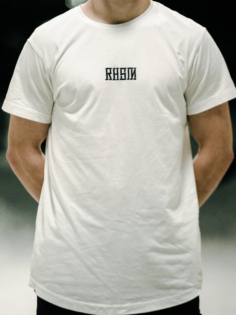 Model wearing the white RHSM Long Fit Tee V2 outside, showcasing its modern and clean streetwear style.