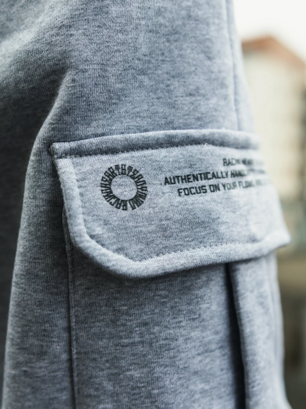 An outdoor close-up of the secure latch on the side cargo pocket of the gray RHSM Sweatpants.