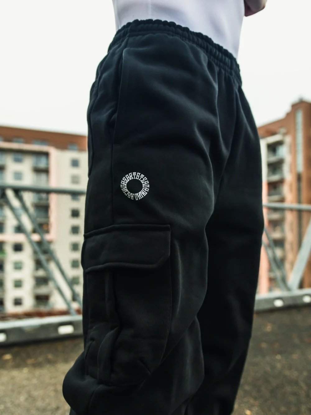 An outdoor close-up shot of a model's hand using the side cargo pocket on the black RHSM Sweatpants.