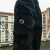 An outdoor close-up shot of a model's hand using the side cargo pocket on the black RHSM Sweatpants.