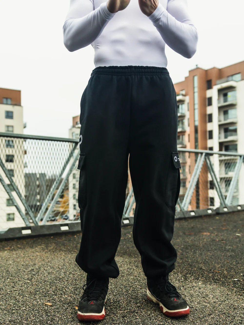 Full front view of a model wearing the black RHSM Cargo Sweatpants in an outdoor setting, showcasing their versatile style.