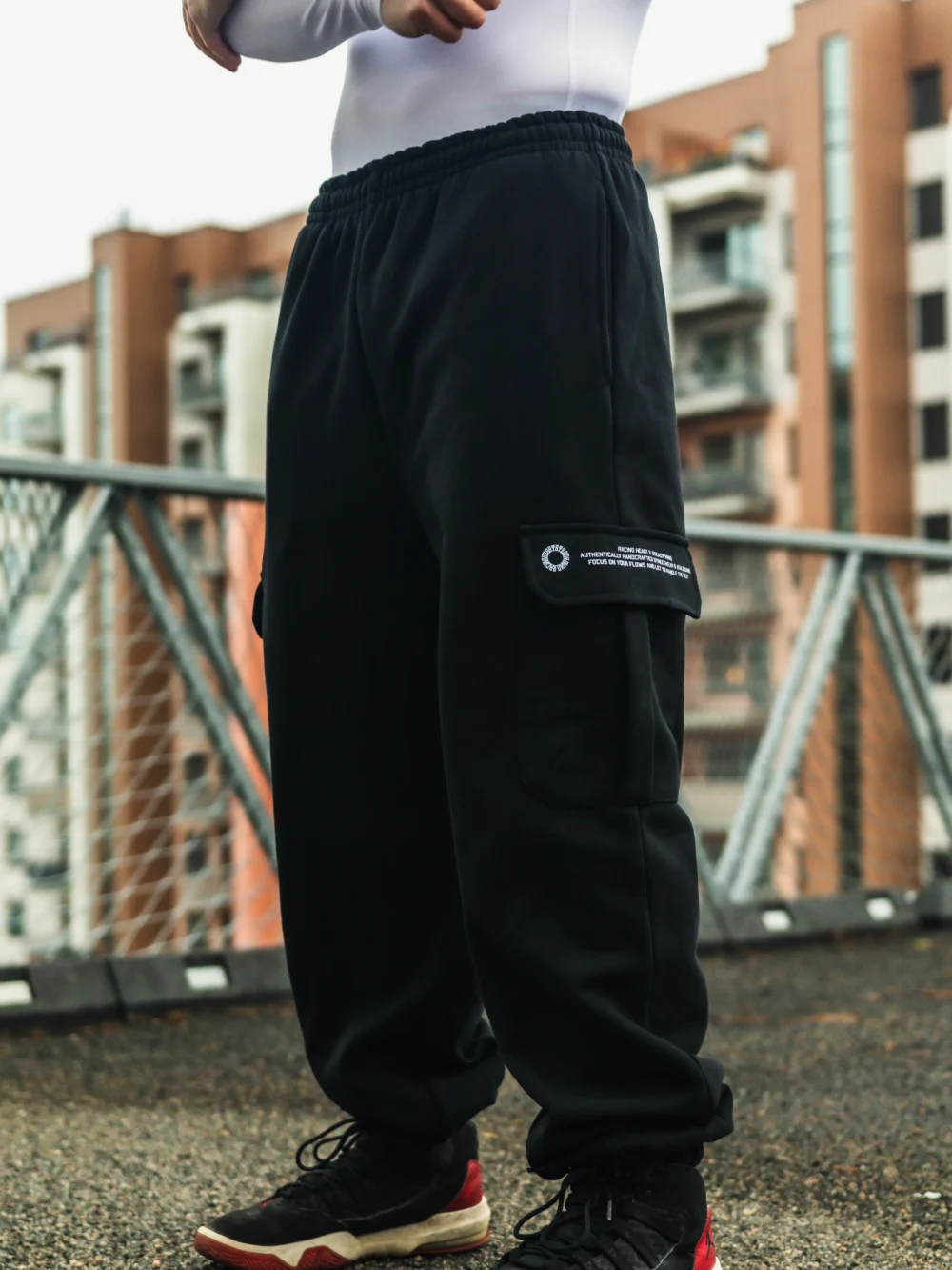 A full side profile of a model wearing the black RHSM Cargo Sweatpants outdoors, highlighting the silhouette and cargo pocket placement.