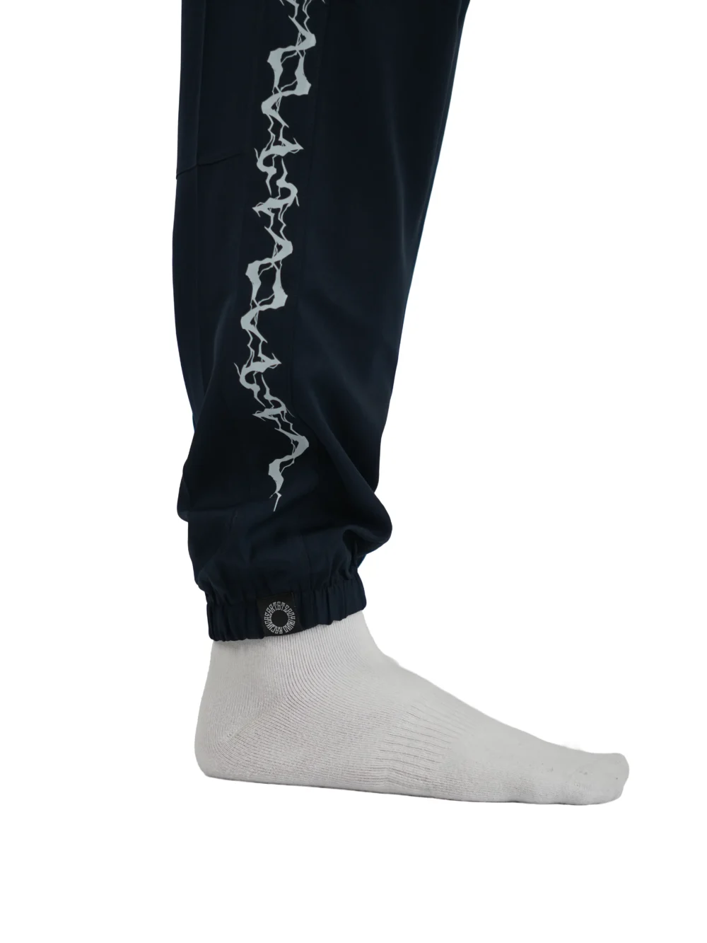 A detailed close-up of the sewn-in RHSM label on the right leg cuff of the navy GODMODE trackpants.