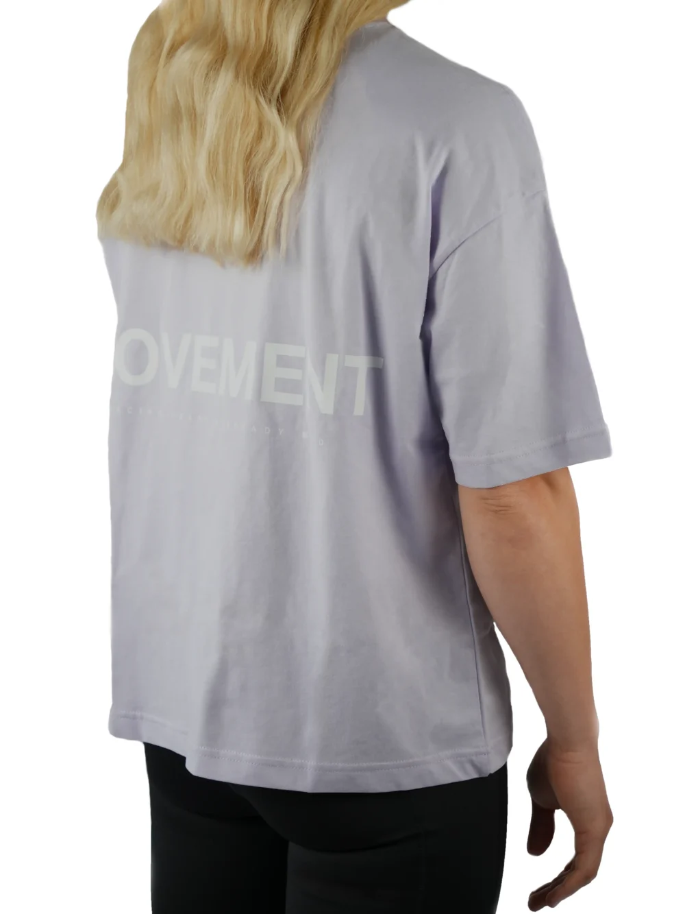 Back view of a female model wearing the lilac oversized boxy tee, showcasing the black "Movement" graphic and the tee's wide, loose fit.