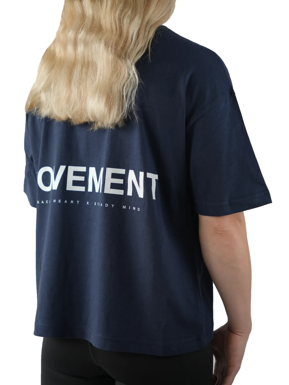 Back view of a female model wearing the navy oversized boxy tee, showcasing the white "Movement" graphic and the tee's wide, loose fit.