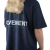 Back view of a female model wearing the navy oversized boxy tee, showcasing the white "Movement" graphic and the tee's wide, loose fit.