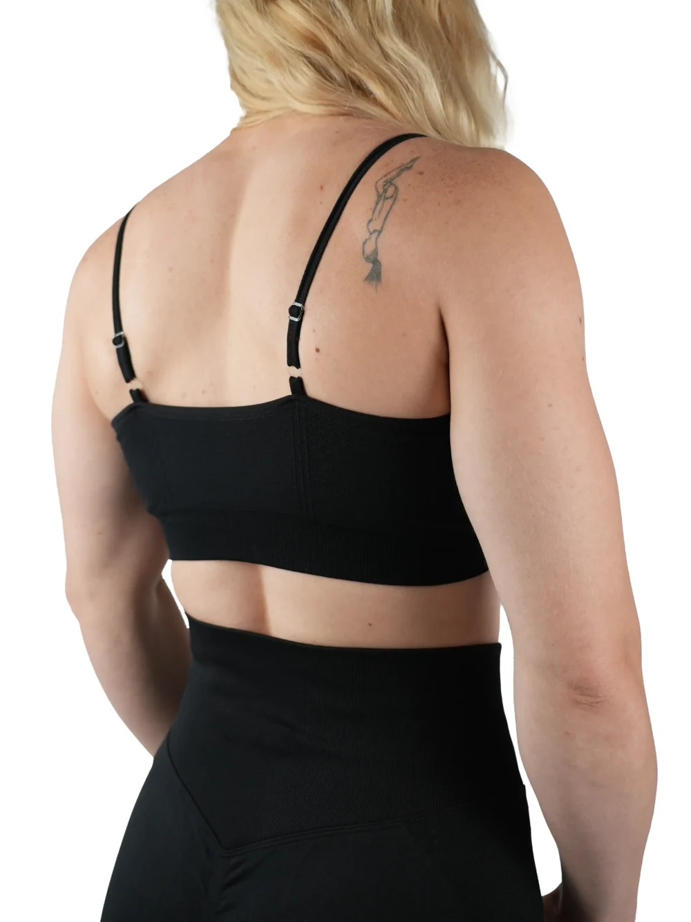 Model wearing the black "[RHXSM]" sports bra (back view), showcasing the adjustable straps and ribbed back design from the calisthenics clothing brand RHSM.
