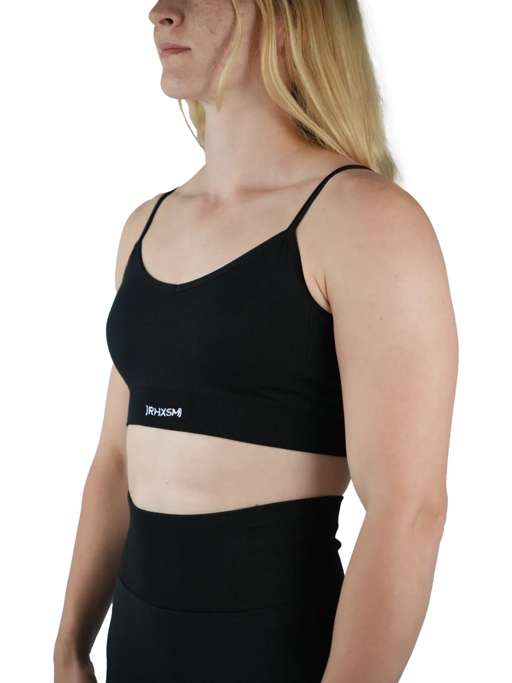 Model wearing the black "[RHXSM]" seamless sports bra (front view), demonstrating the supportive, medium-impact fit of this women's workout gear.