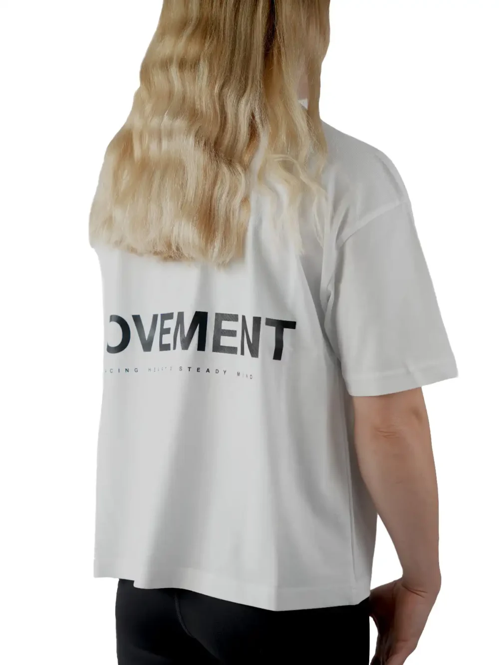 Back view of a female model wearing the white oversized boxy tee, showcasing the black "Movement" graphic and the tee's wide, loose fit.