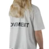 Back view of a female model wearing the white oversized boxy tee, showcasing the black "Movement" graphic and the tee's wide, loose fit.