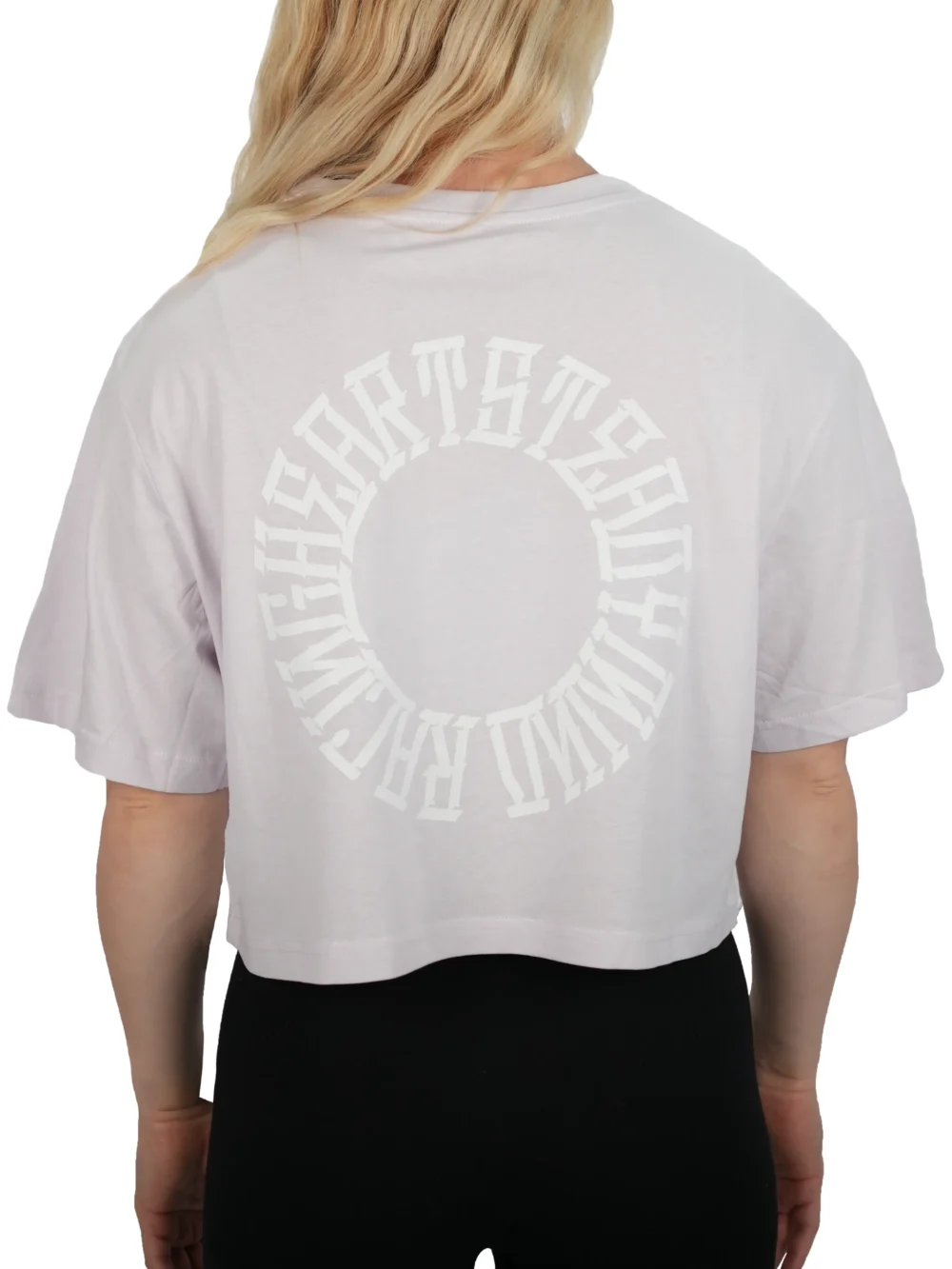 Model turning to show the back of the lilac oversized tee, highlighting the large "Racing Heart Steady Mind" graphic on the RHSM workout gear.