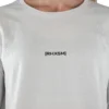 A close-up of the white "[RHXSM]" long sleeve tee, showing the clean front graphic and premium sewn-in label from the calisthenics clothing brand RHSM.