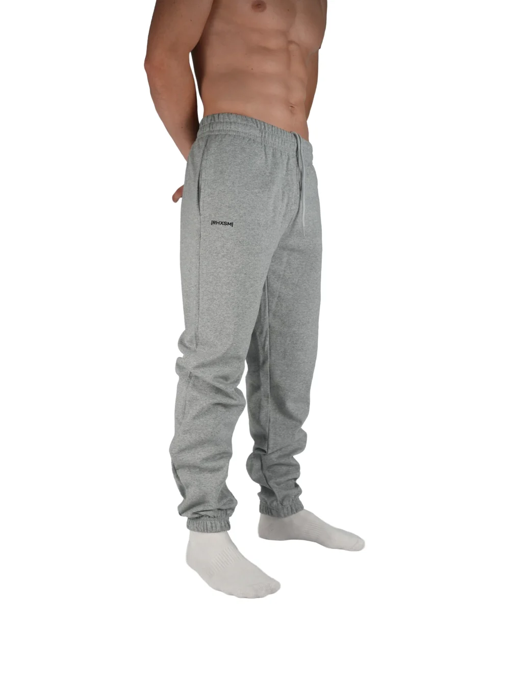 A close-up of the RHSM "[RHXSM]" sweatpants in grey, showing the small, subtle graphic on the right side pocket from the calisthenics clothing brand.