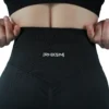 A close-up of the black "[RHXSM]" seamless leggings, detailing the premium embroidered back graphic with its anti-scratch interior backing for comfort.