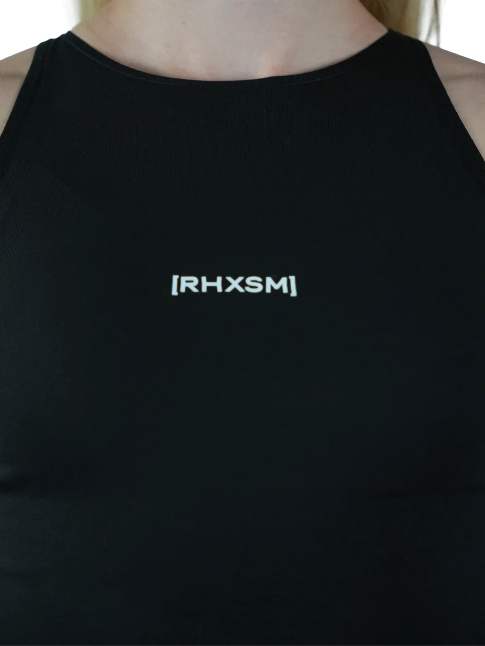 A close-up of the black "[RHXSM]" crop top, detailing the subtle front graphic and sewn-in hem label on this piece of performance apparel.