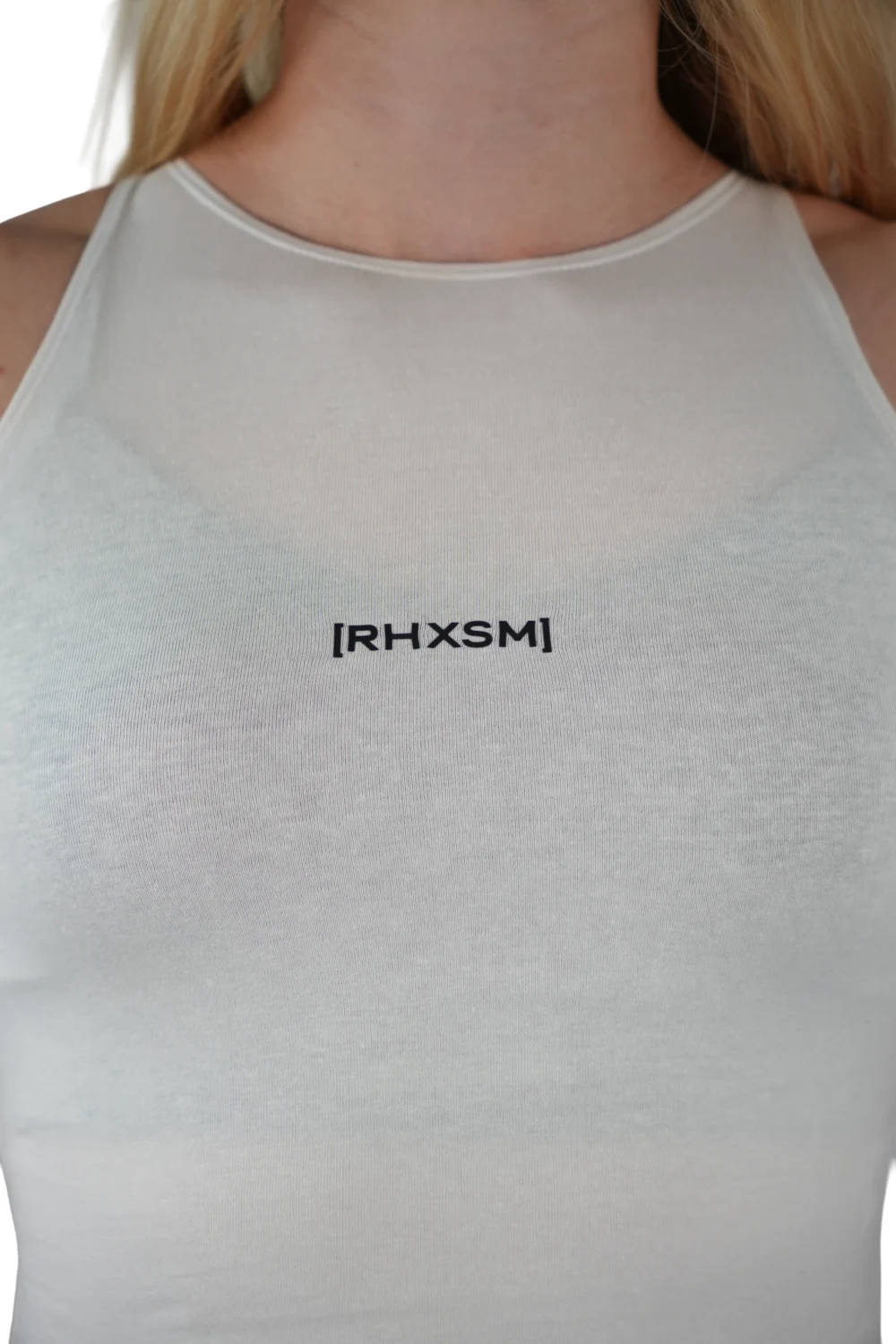 A close-up of the white "[RHXSM]" crop top, showing the clean front graphic and premium sewn-in label from the calisthenics clothing brand RHSM.
