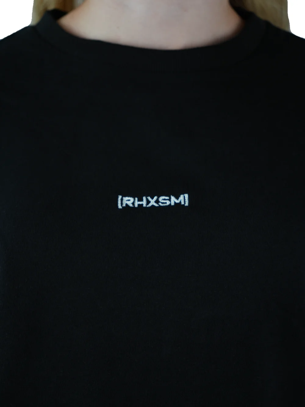 A close-up of the black "[RHXSM]" cropped crew, detailing the premium embroidered front graphic and sewn-in hem label on this piece of performance apparel.