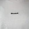 A close-up of the white "[RHXSM]" cropped crew, showing the clean embroidered graphic and premium sewn-in label from the calisthenics clothing brand RHSM.