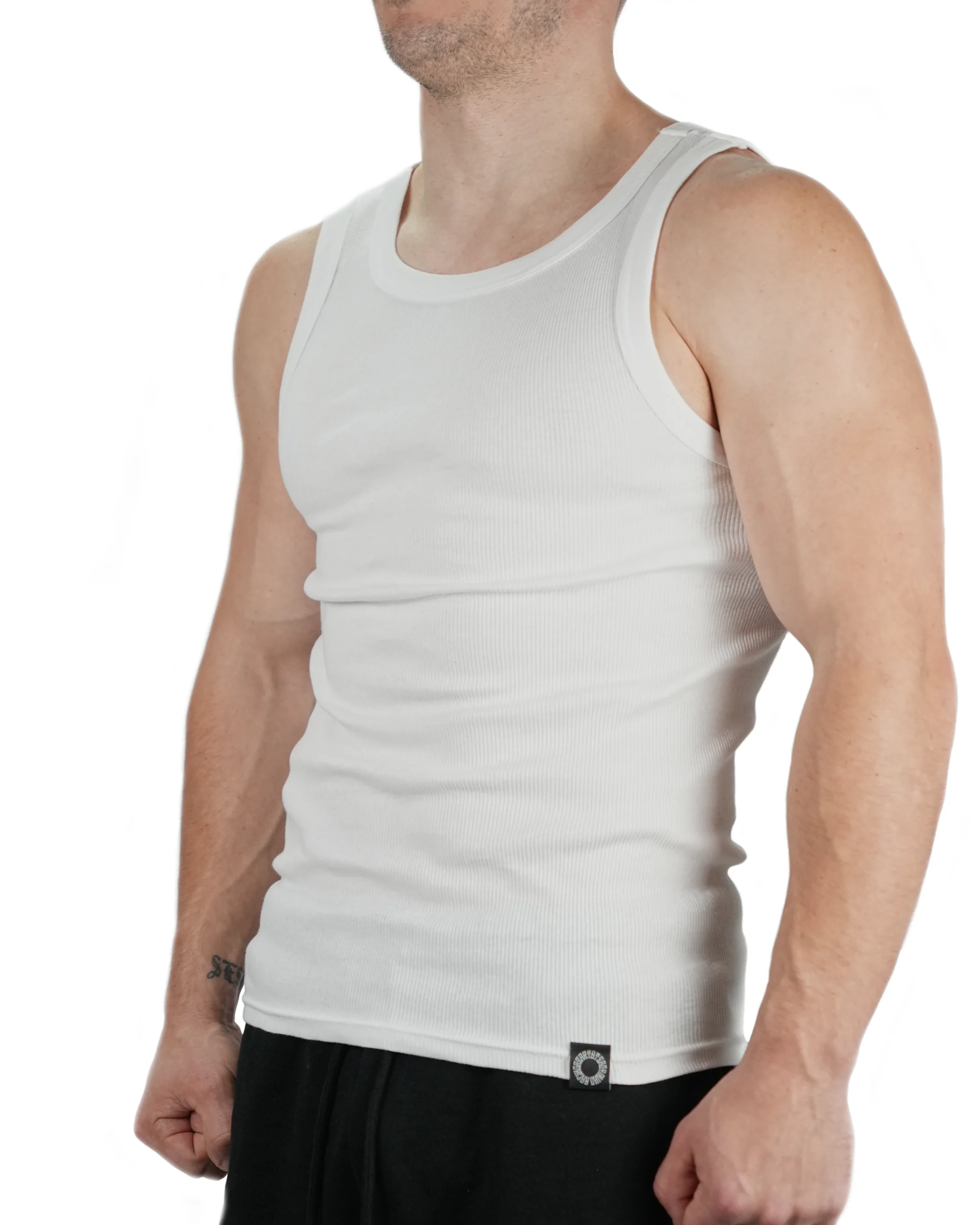 Muscular male model wearing white RHSM Minimalist Ribbed Tank, showing the form-fitting structure and small hem tag for workout gear.